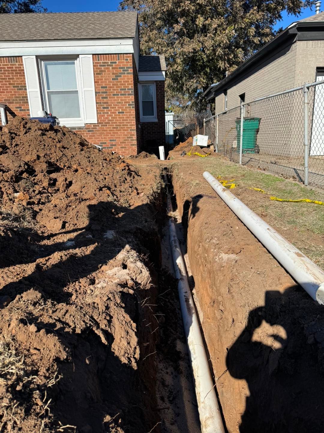 A drain pipe is being installed in the dirt in front of a house.