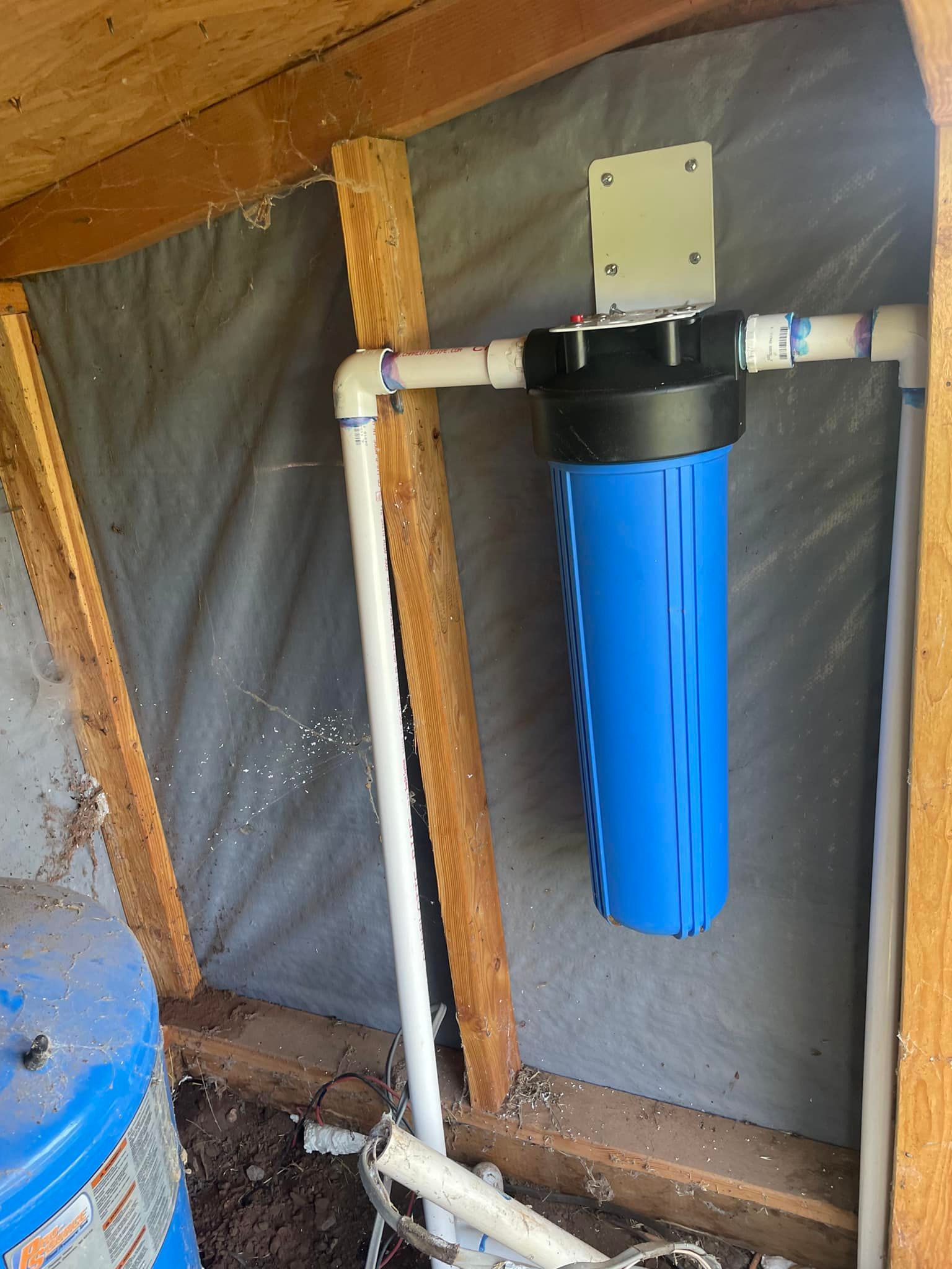 A blue water filter is hanging from a pipe in a shed.