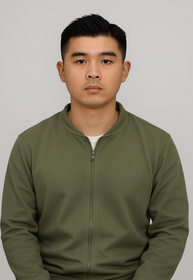 Man in grey blazer smiling, seated indoors near a window.