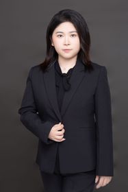 Man in grey blazer smiling, seated indoors near a window.