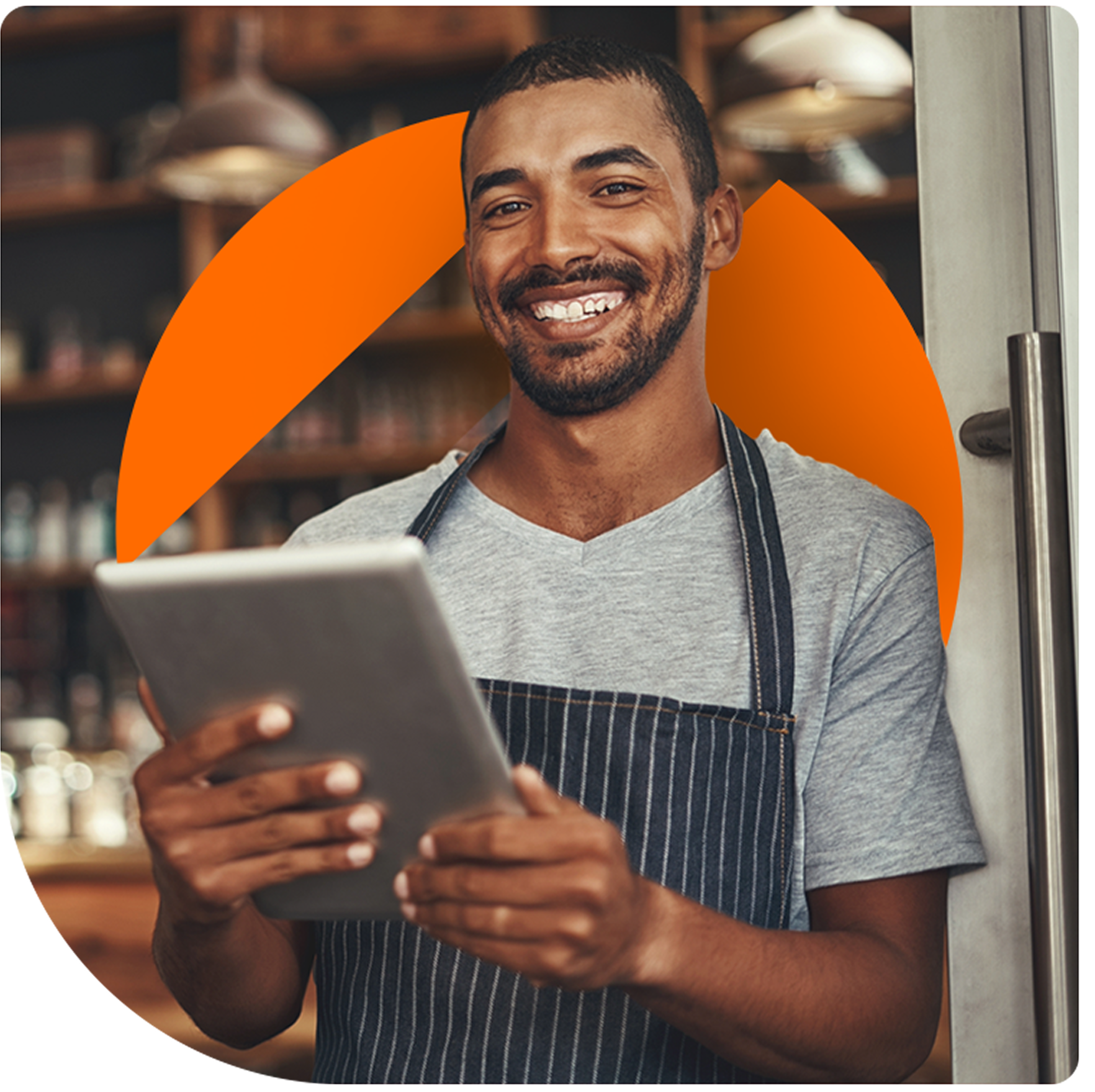 Man in apron smiles, holds tablet near a doorway, with orange circle overlay.