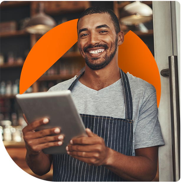 Man in apron smiles, holds tablet near a doorway, with orange circle overlay.