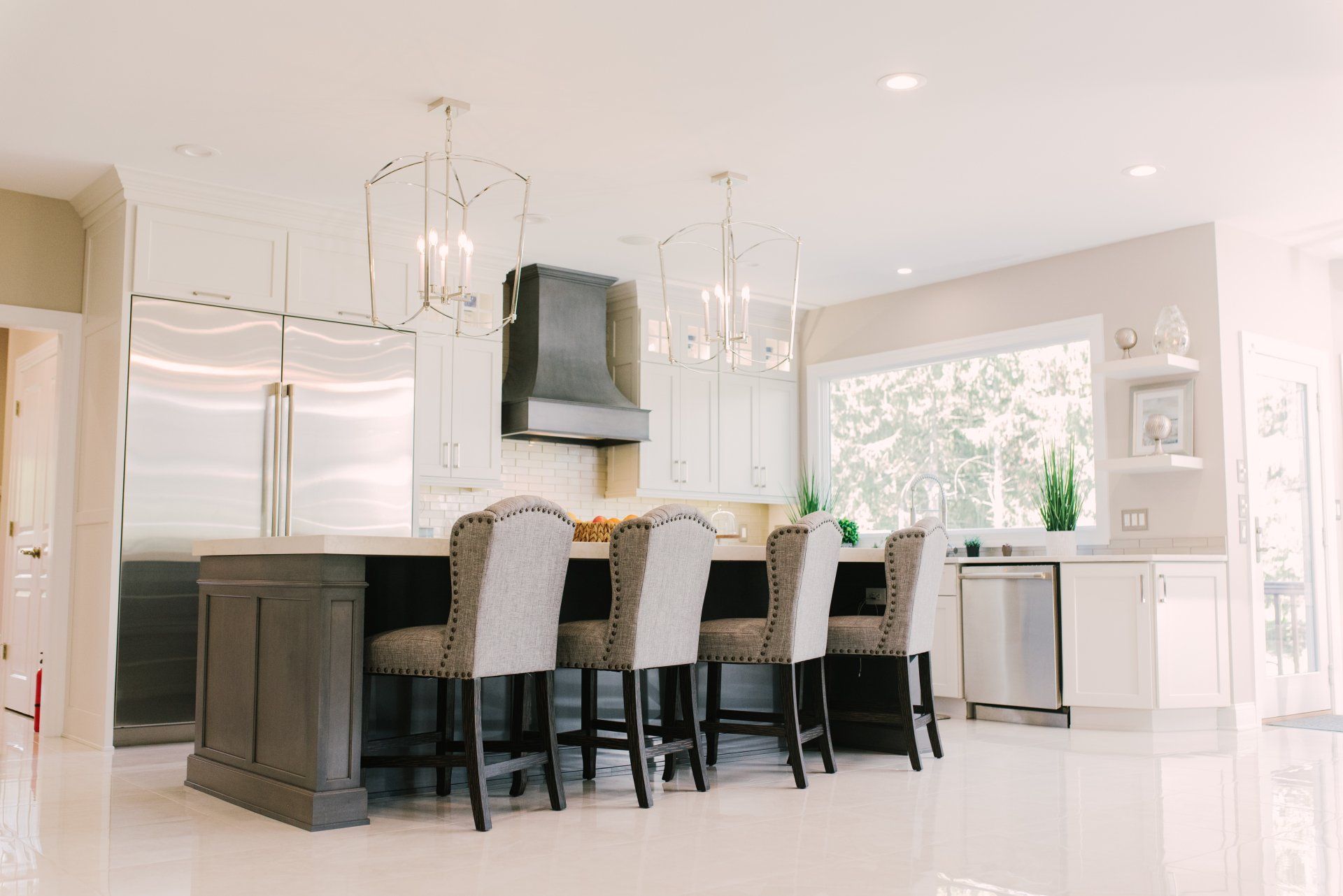 A kitchen with white cabinets , stainless steel appliances , a large island and chairs.