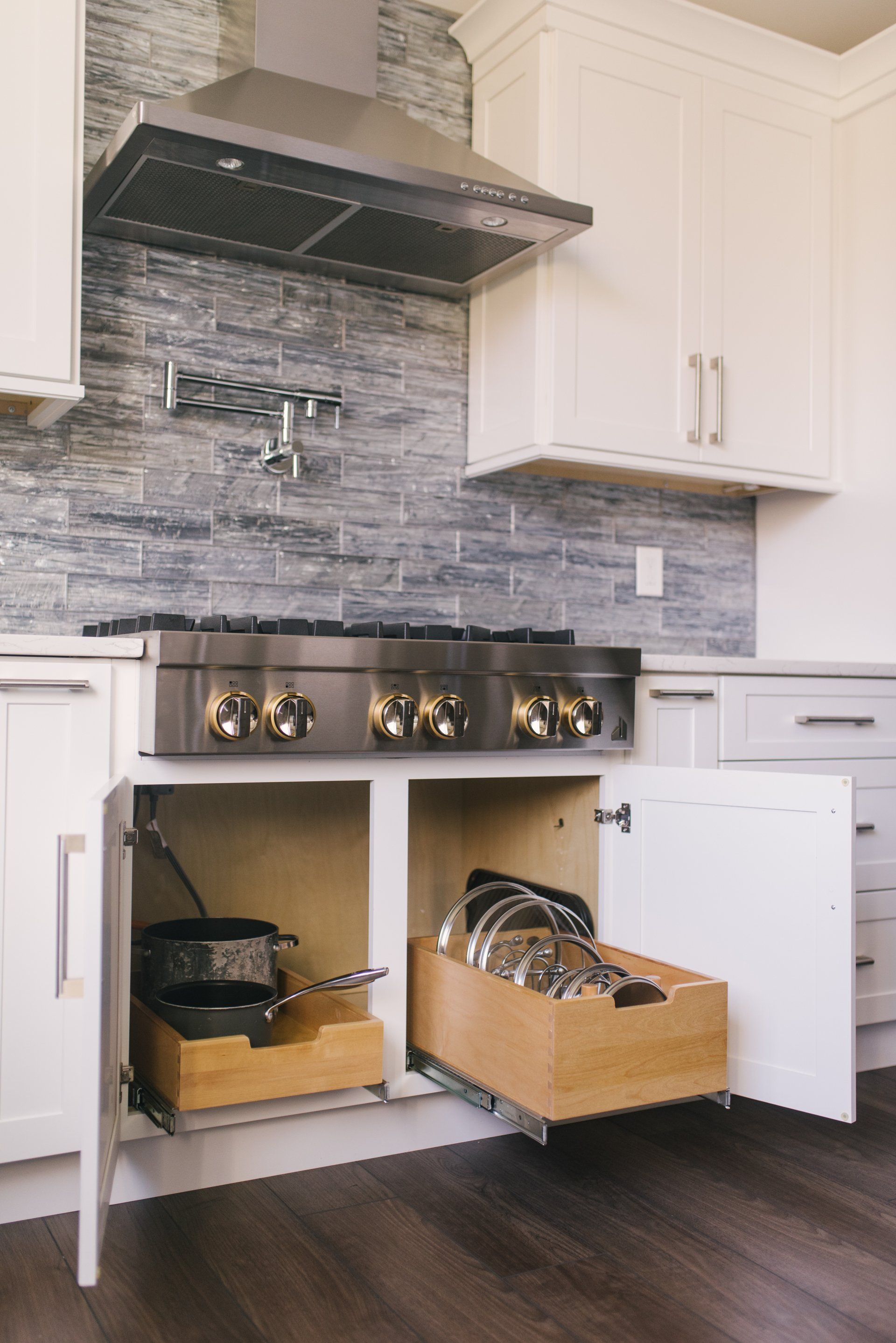 A kitchen with a stove and a drawer filled with pots and pans