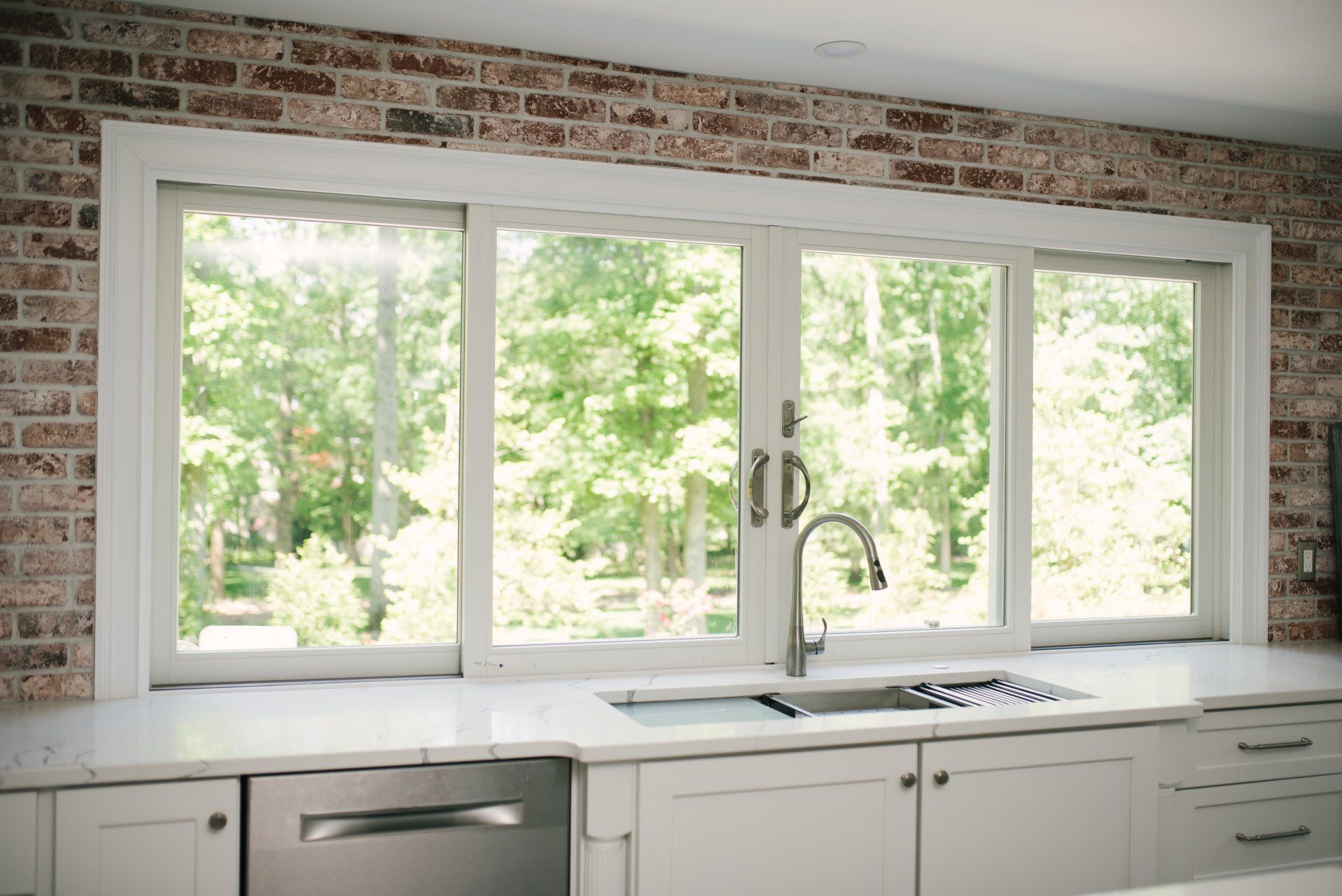 A kitchen with a sink , dishwasher , and large windows.