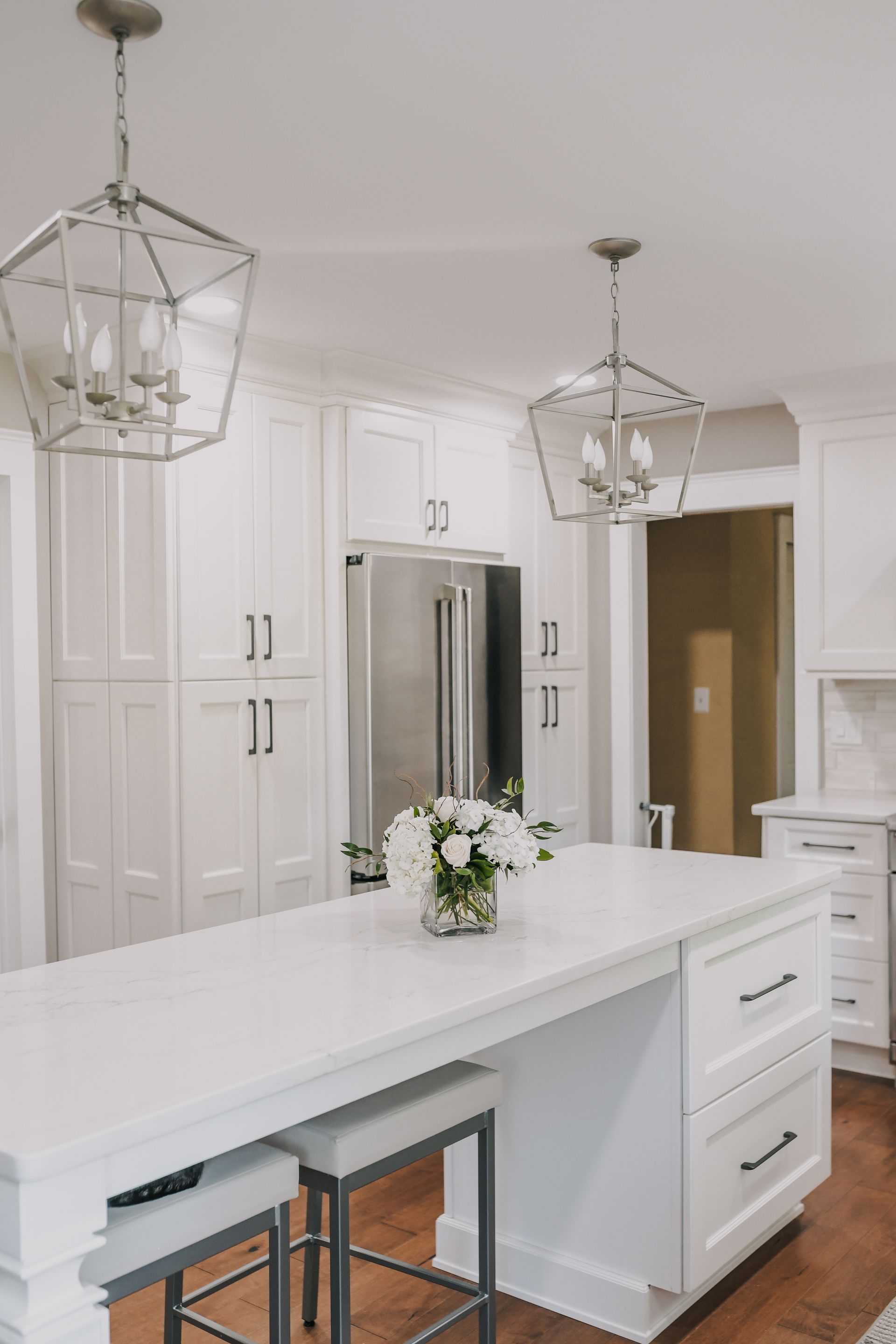 A kitchen with white cabinets and a large island with a vase of flowers on it.