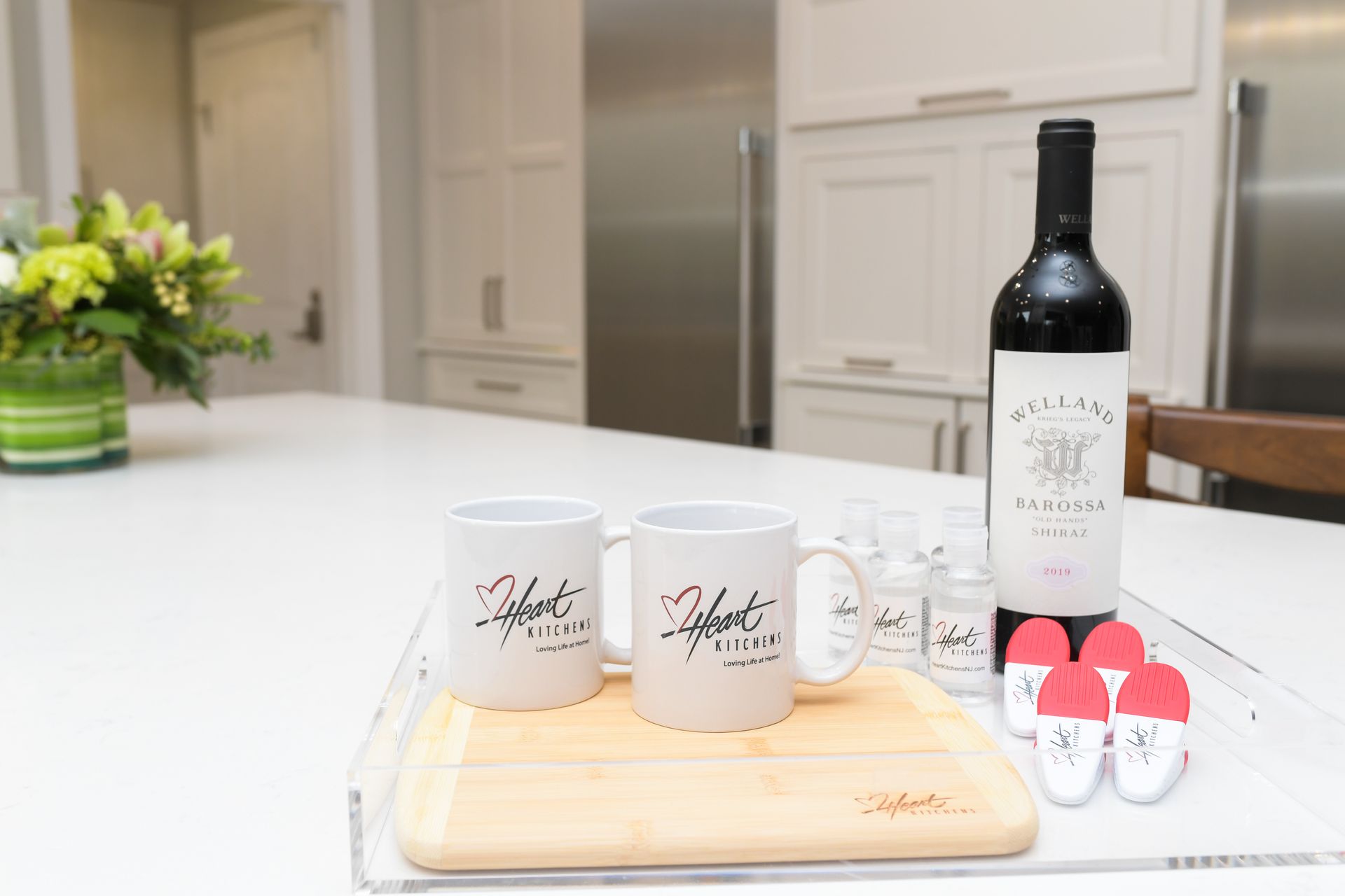 A bottle of wine and two mugs are on a tray on a kitchen counter.