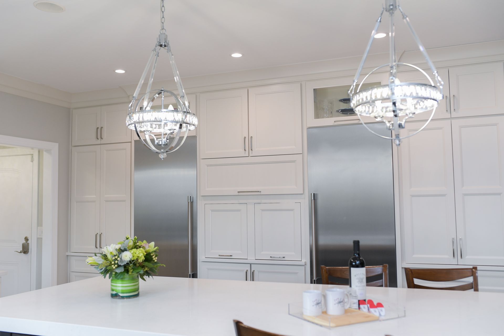 A kitchen with white cabinets , stainless steel appliances , a bottle of wine and a vase of flowers.