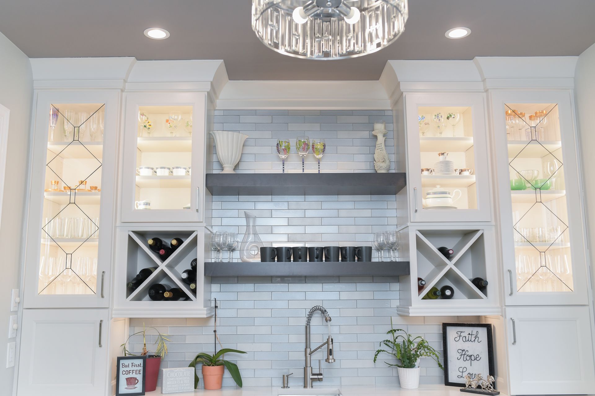 A kitchen with white cabinets , a sink , a wine rack and a chandelier.