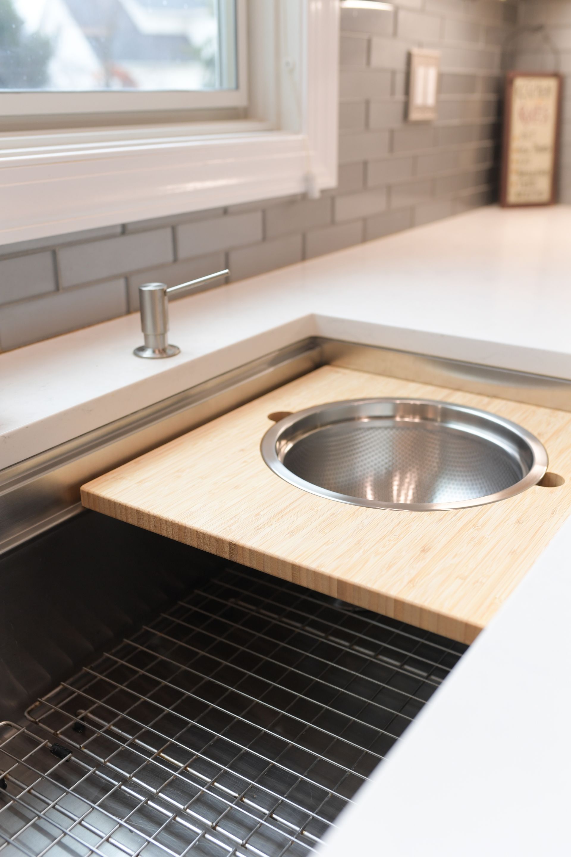 A kitchen sink with a wooden cutting board underneath it.