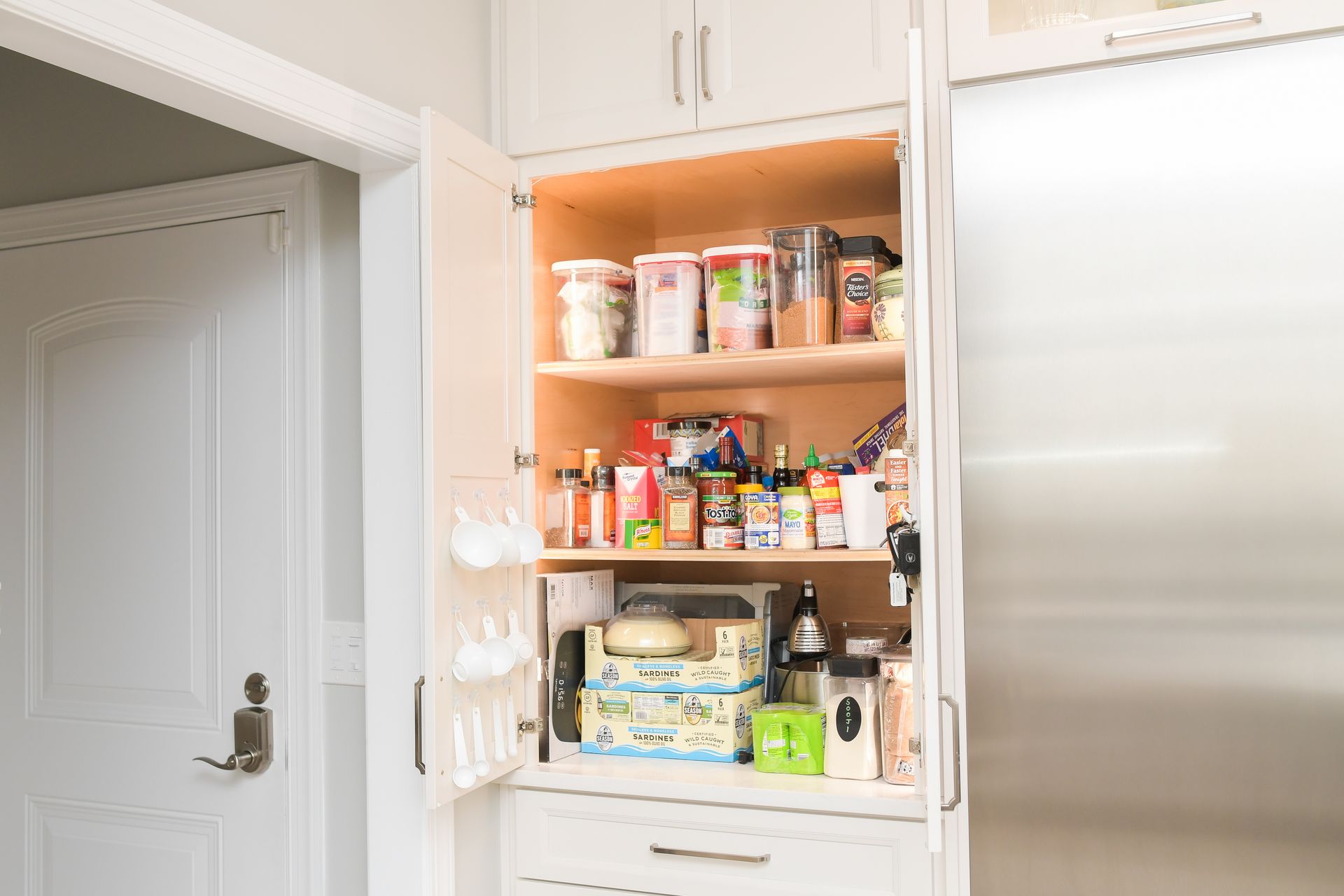 A pantry in a kitchen with the door open and lots of food on the shelves.