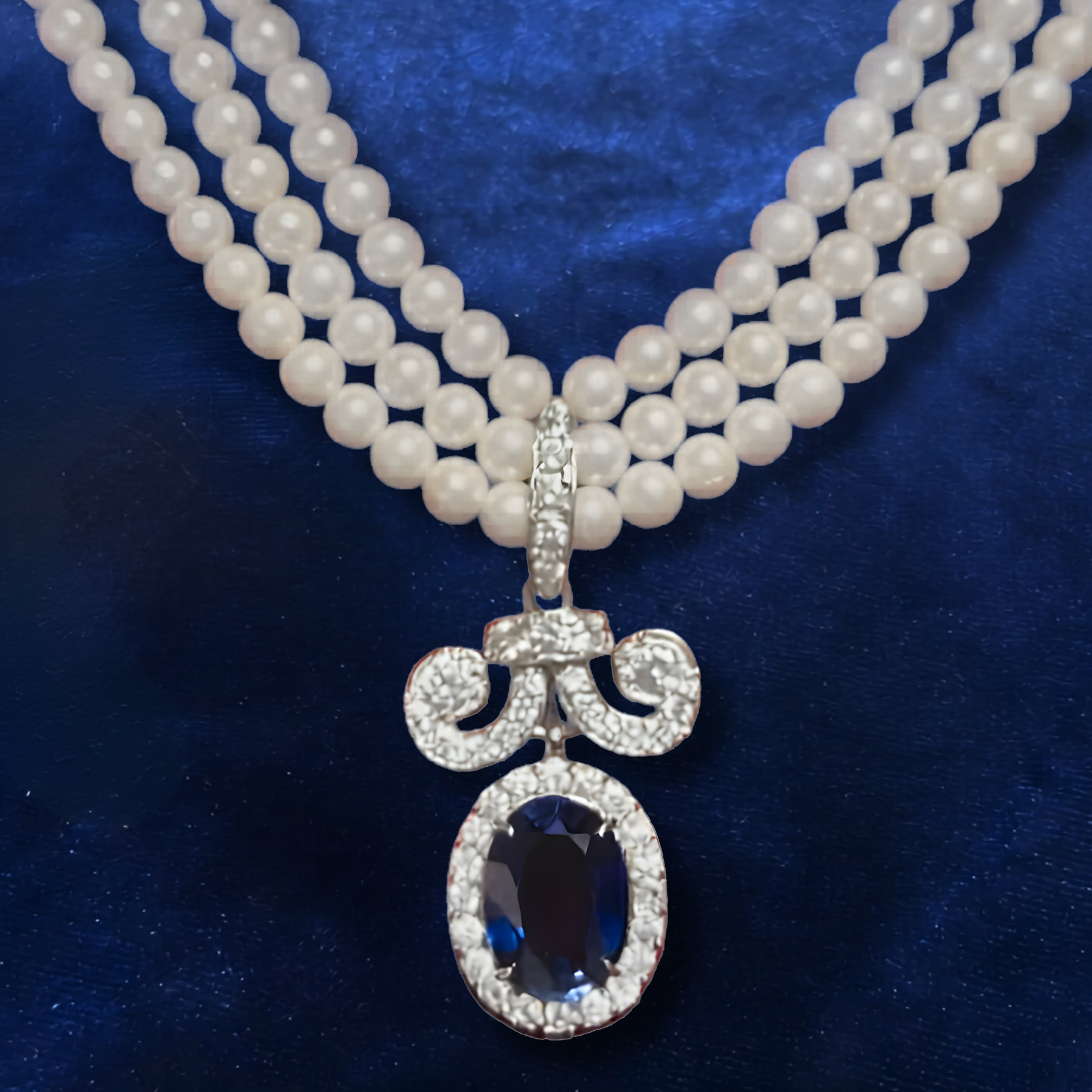 A triple-strand pearl necklace with a pendant featuring a central oval blue sapphire surrounded by clear pavé stones.