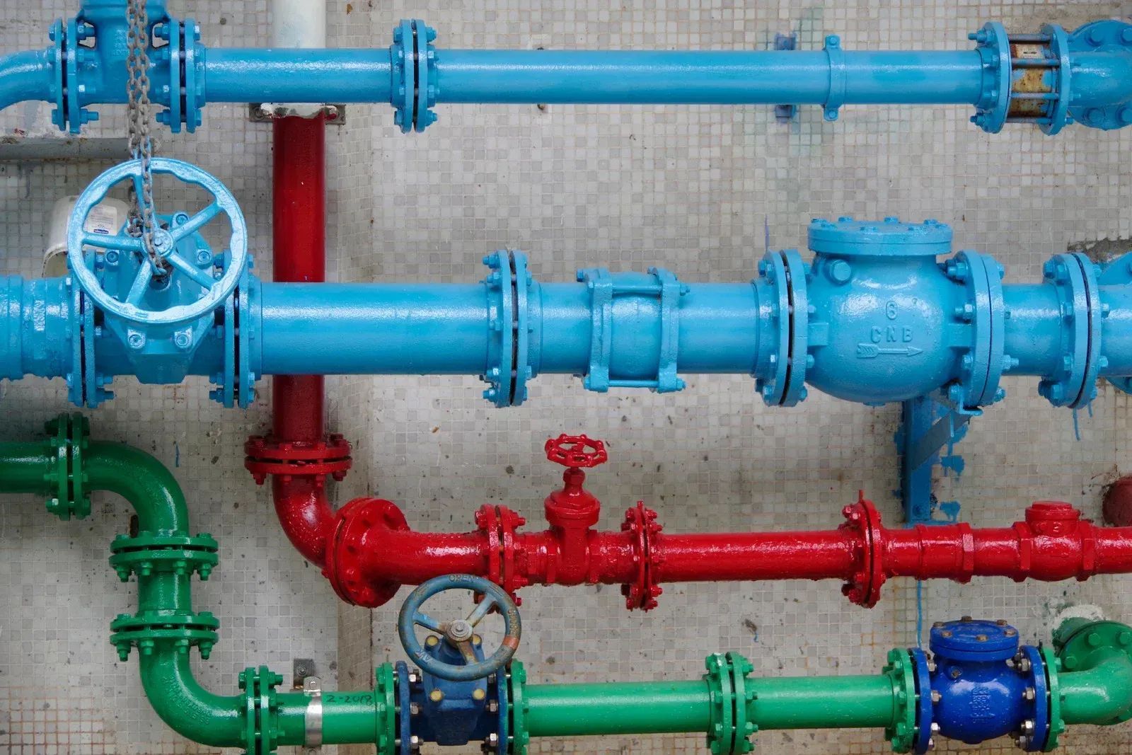 Colorful pipes and valves against a concrete wall.