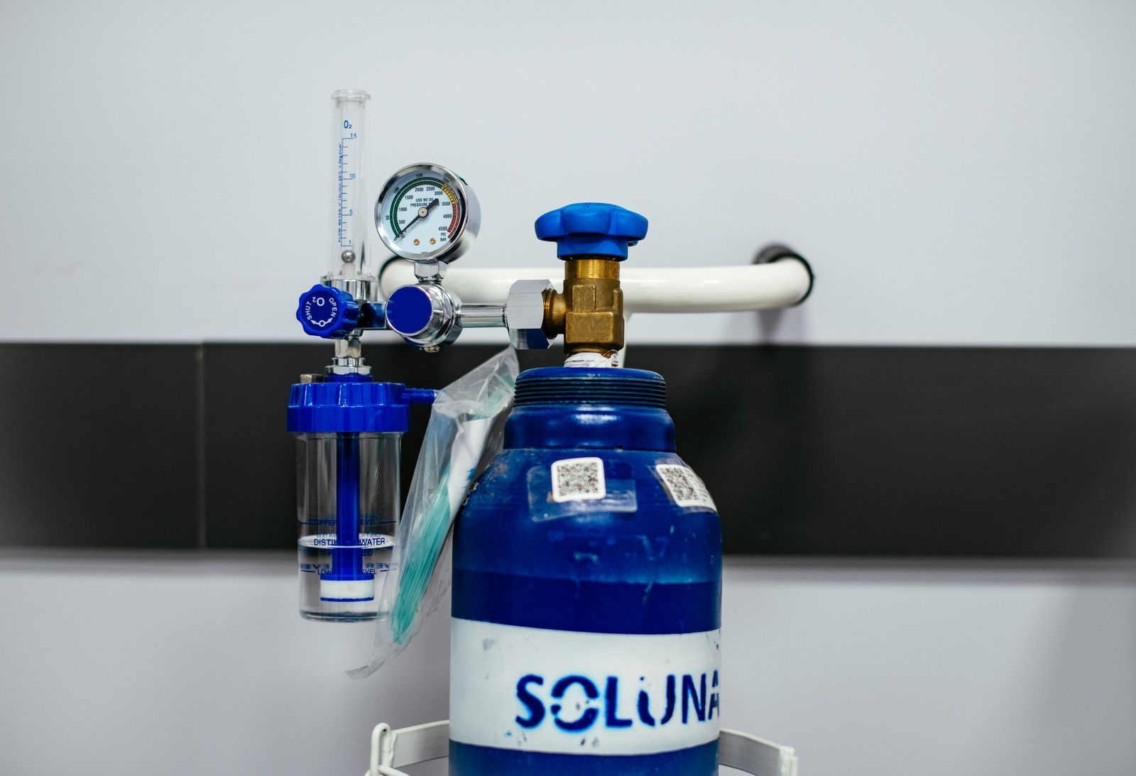 Blue oxygen tank with a gauge and flow meter mounted on a wall, labeled 