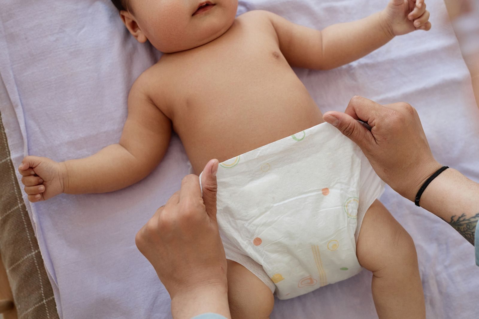 A woman is changing a baby 's diaper on a bed.