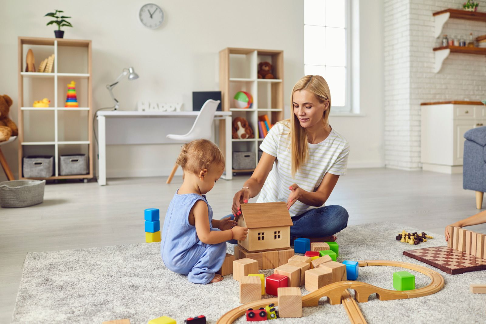A woman and a little girl are sitting on the floor playing with wooden blocks.