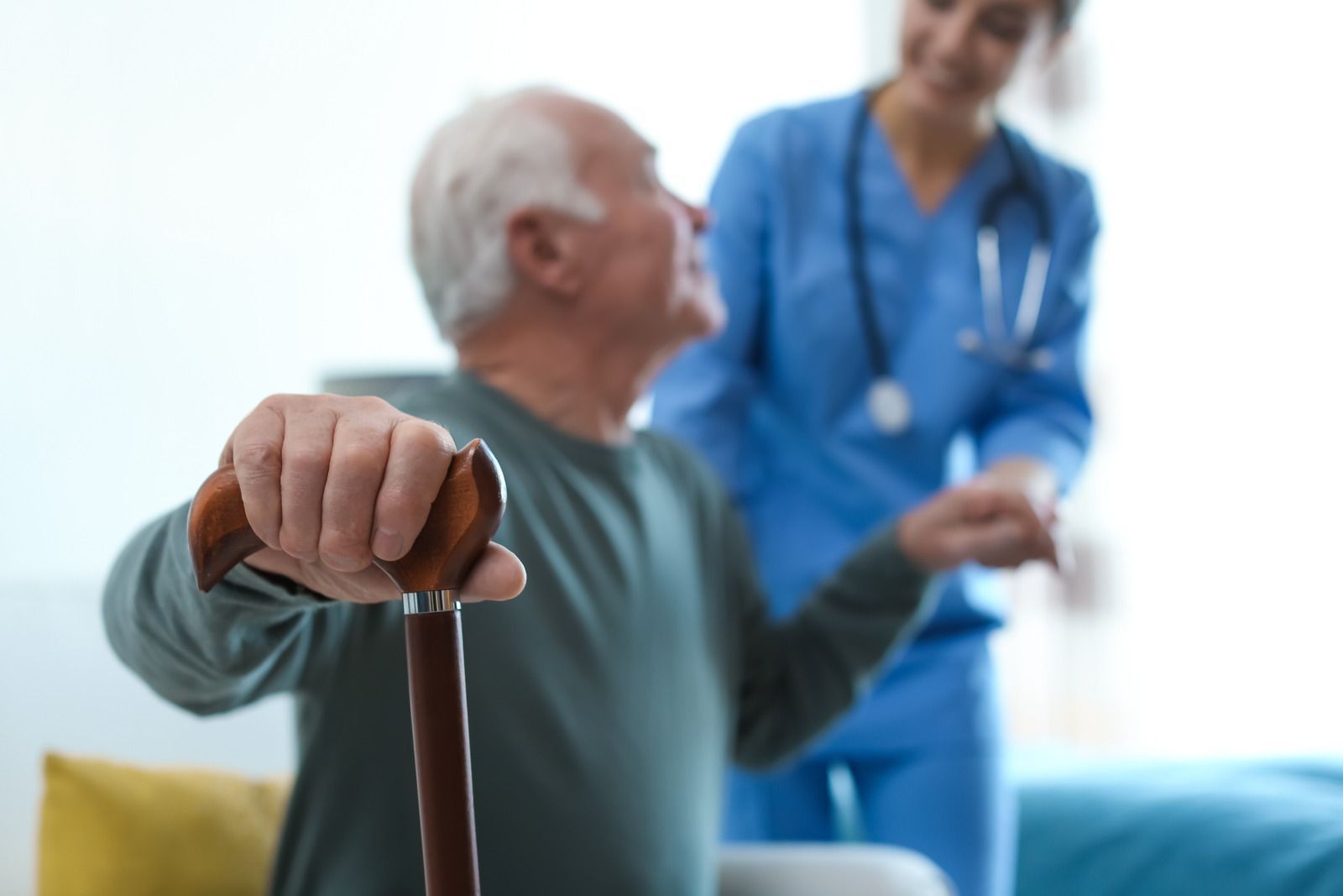 An elderly man with a cane is being helped by a nurse.
