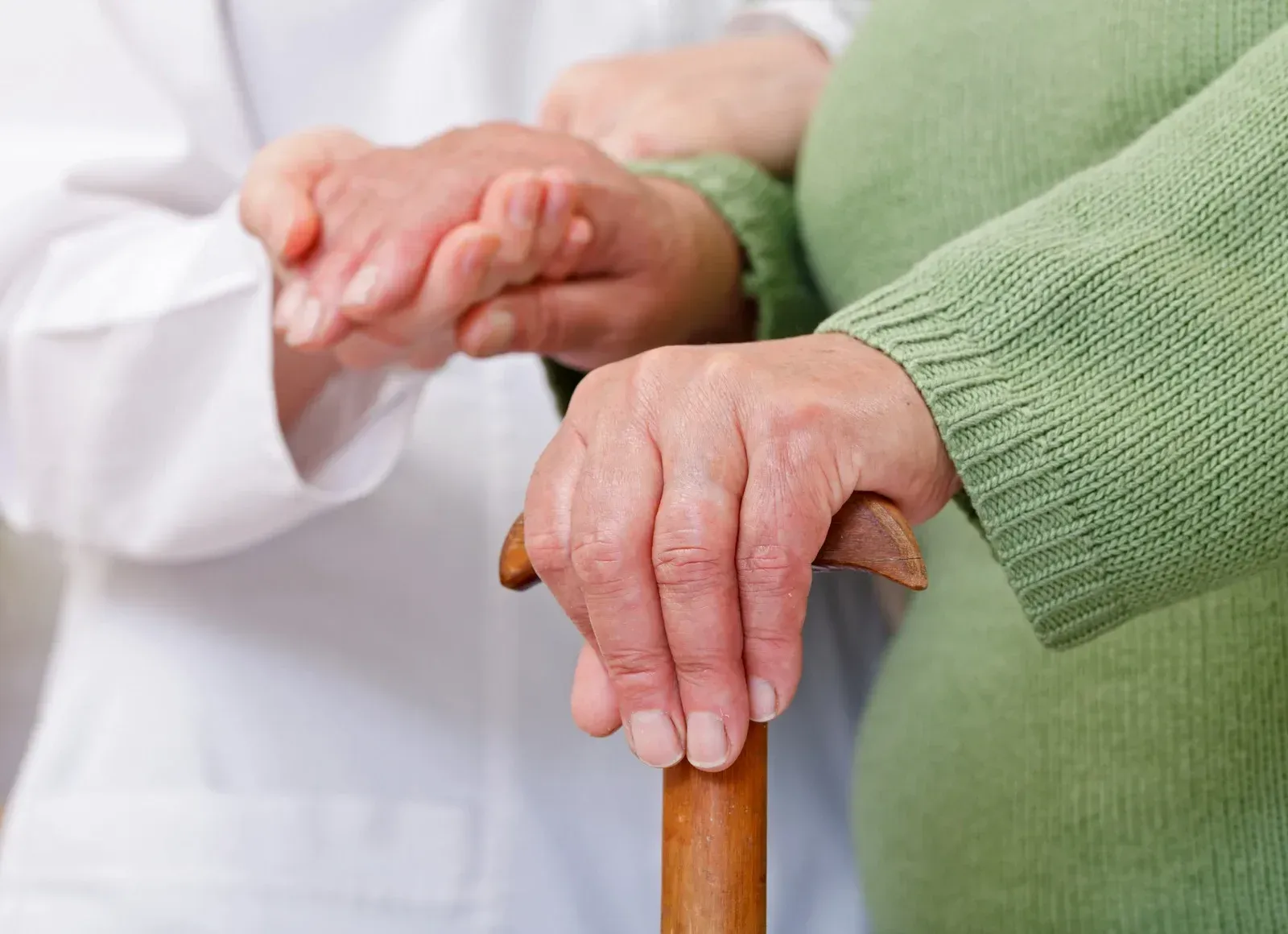 A nurse is holding the hand of an elderly woman holding a cane.