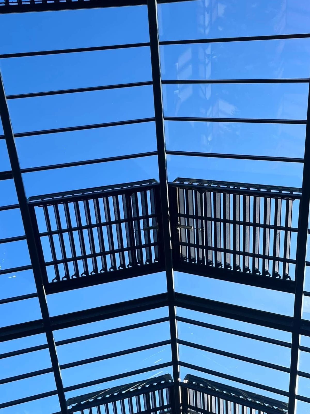 Blauwe lucht zichtbaar door een zwart dak van metaal en glas met schaduwpanelen.
