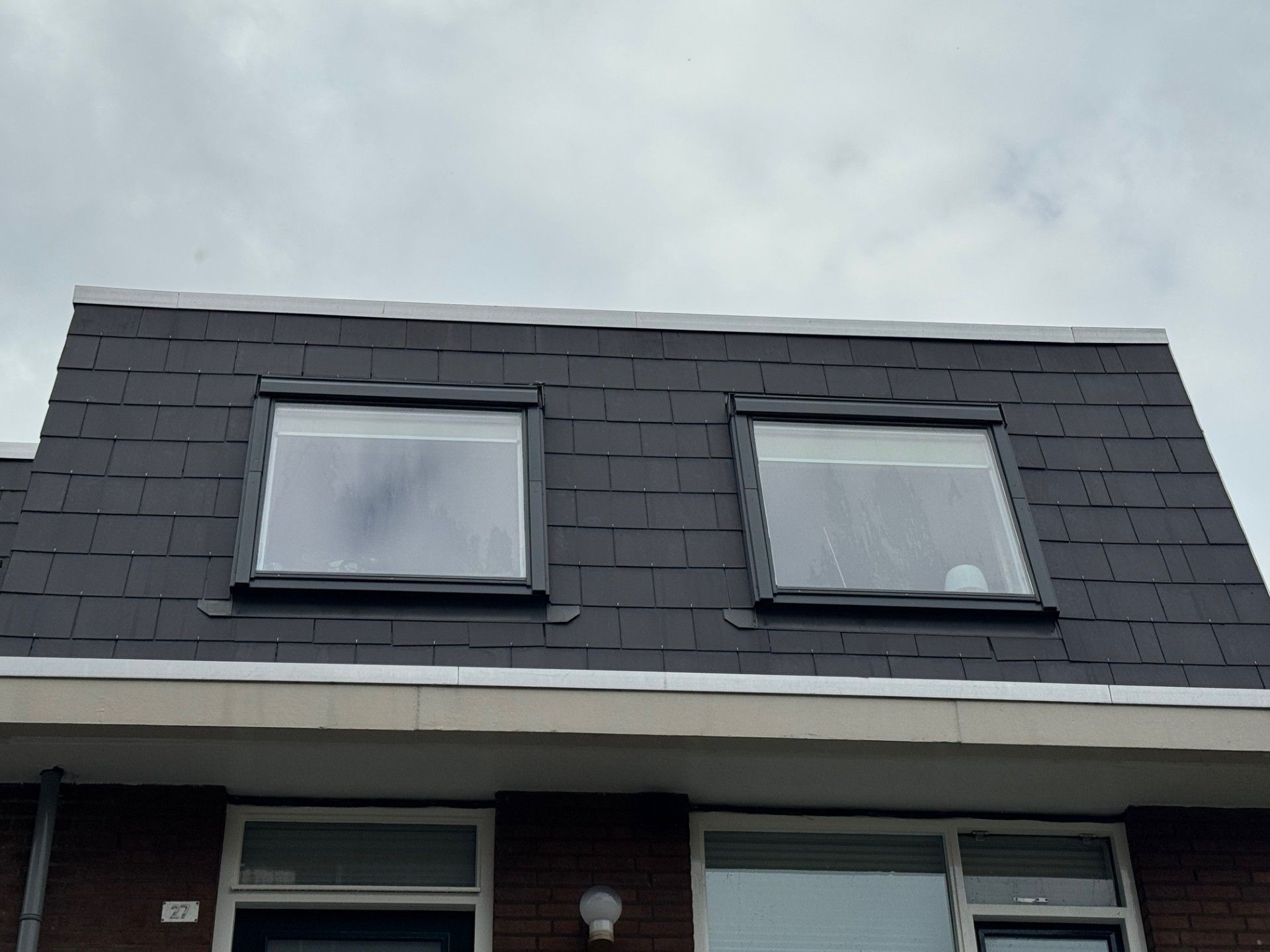 Donkergrijs dak met twee vierkante ramen, grijze afwerking, bewolkte lucht.