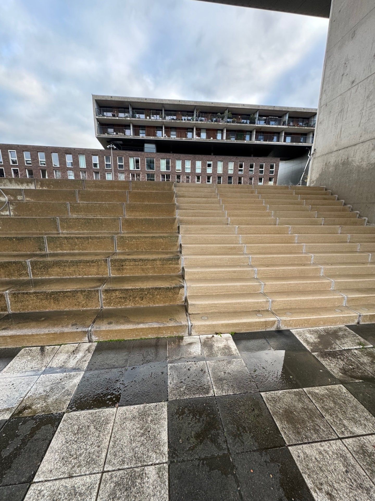 Stenen trappen leiden naar een gebouw met balkons. De trap is nat.