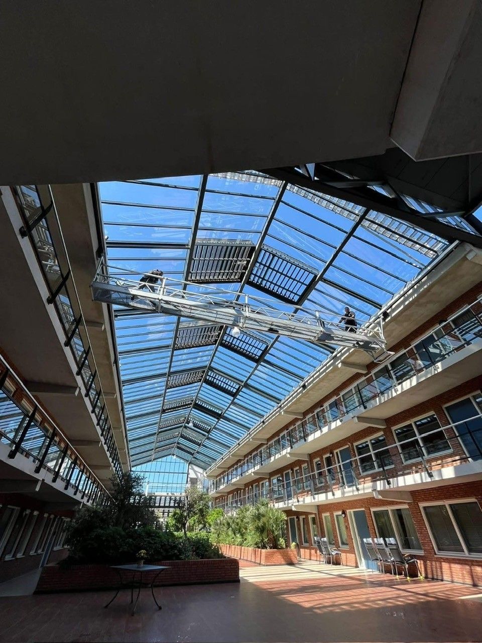 Interieur van een gebouw met een glazen dak, kijkend naar de lucht. Gebouw met meerdere verdiepingen en een centrale tuin.