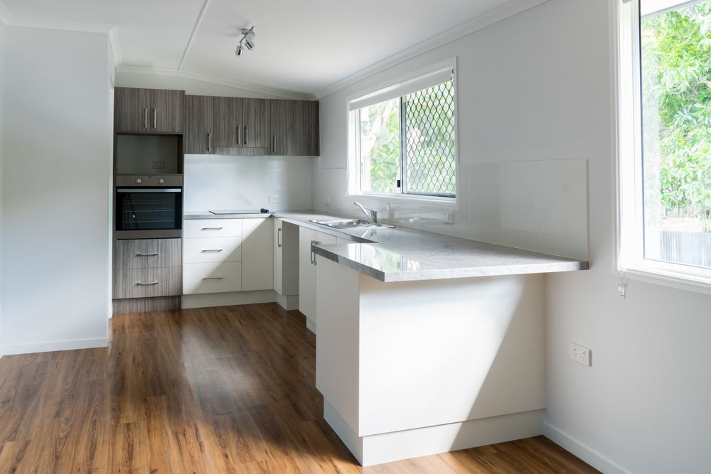 An Empty Kitchen With White Cabinets and Wooden Floors — Pacific Cabinets In Evans Head, NSW