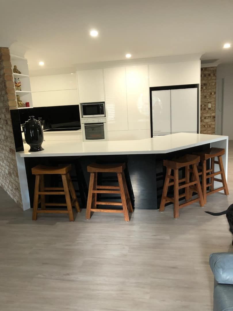A Kitchen With a Large Island and Wooden Stools — Pacific Cabinets In Maclean, NSW