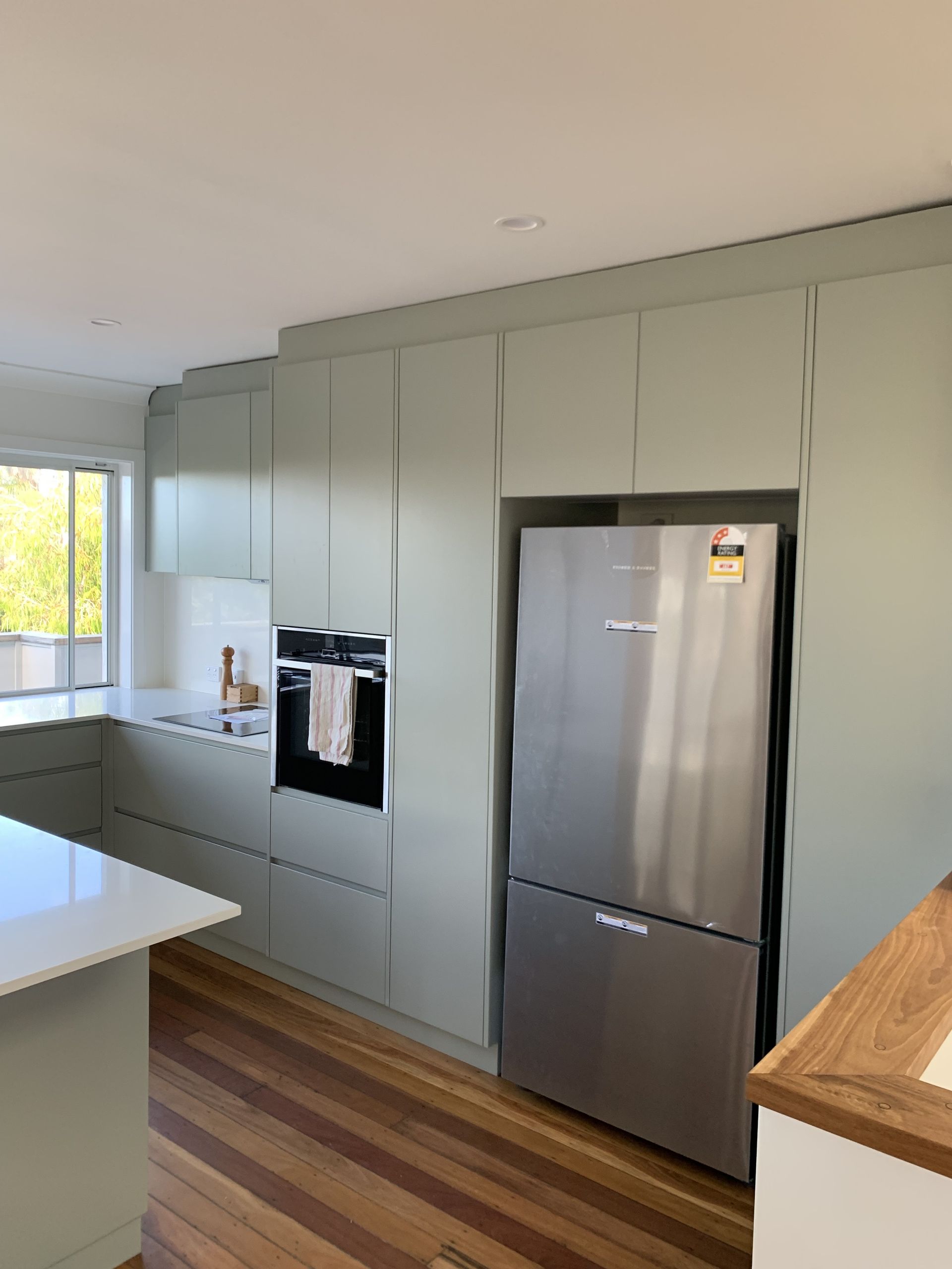 Kitchen with light green cabinets, stainless steel refrigerator, and wooden floors — Pacific Cabinets In Yamba, NSW