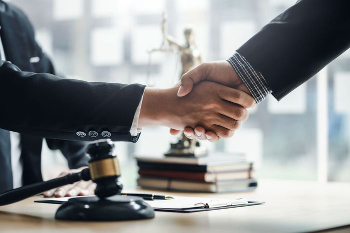 Two men are shaking hands in front of a judge 's gavel in a courtroom.