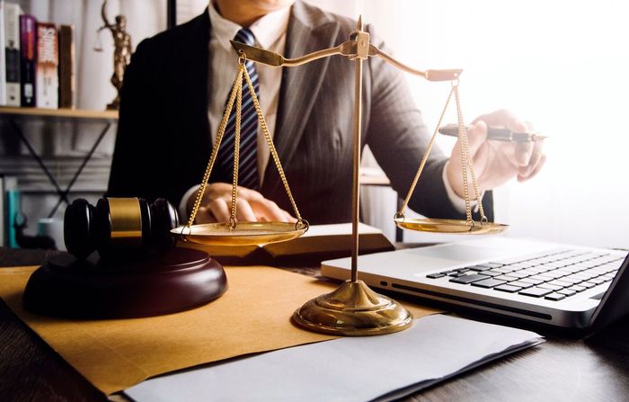 A lawyer is sitting at a desk with a scale of justice and a laptop.