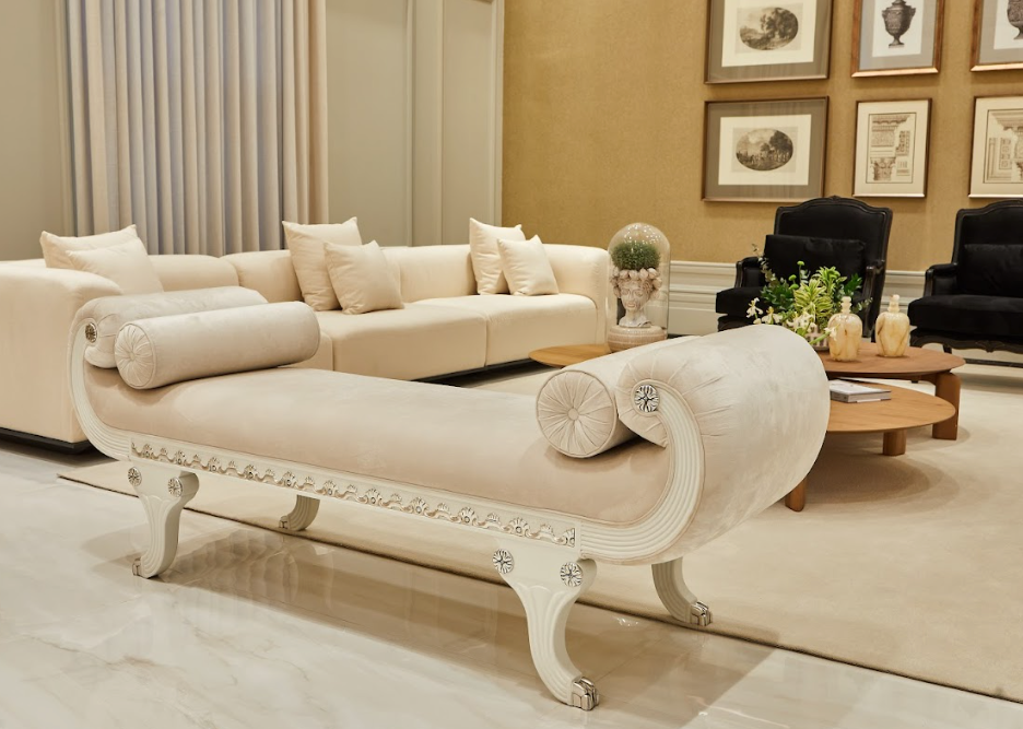 Sala de estar em tons de creme com um banco curvo, sofá secional, poltronas pretas e mesas de centro redondas de madeira.