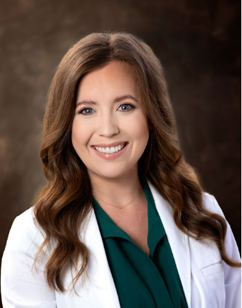 A woman in a white coat and green shirt is smiling for the camera.