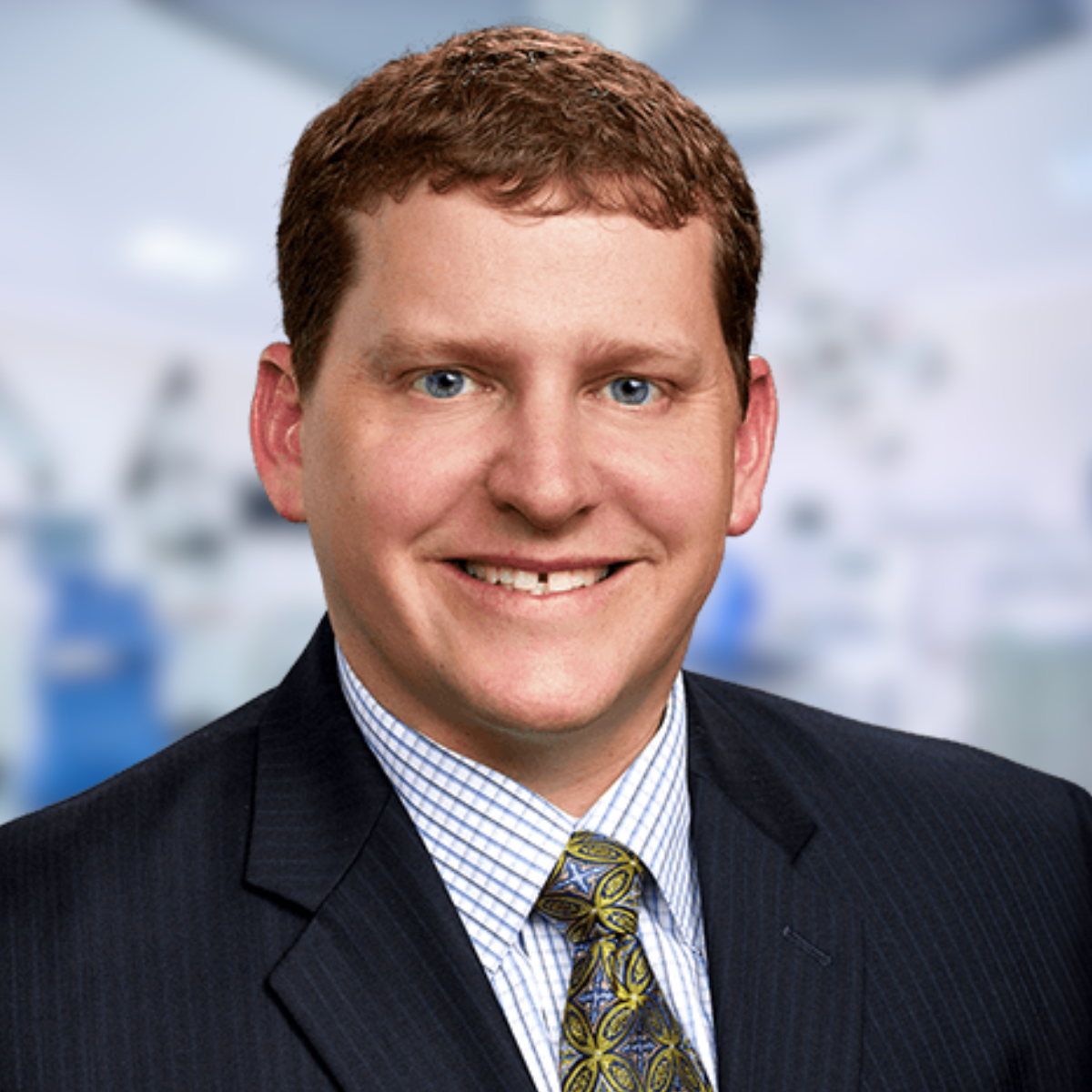 Man in a suit smiles at the camera; background blurred.