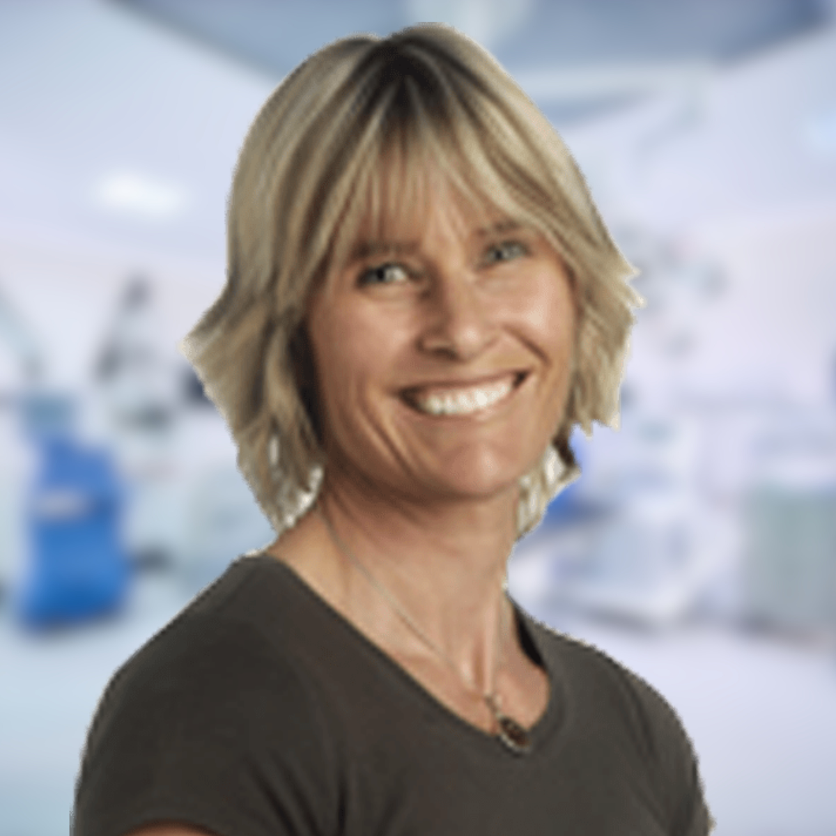 Woman smiling in a hospital setting, wearing a dark top with short blonde hair.
