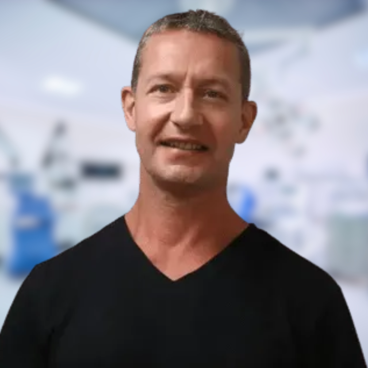 Man in a suit smiles at the camera; background blurred.