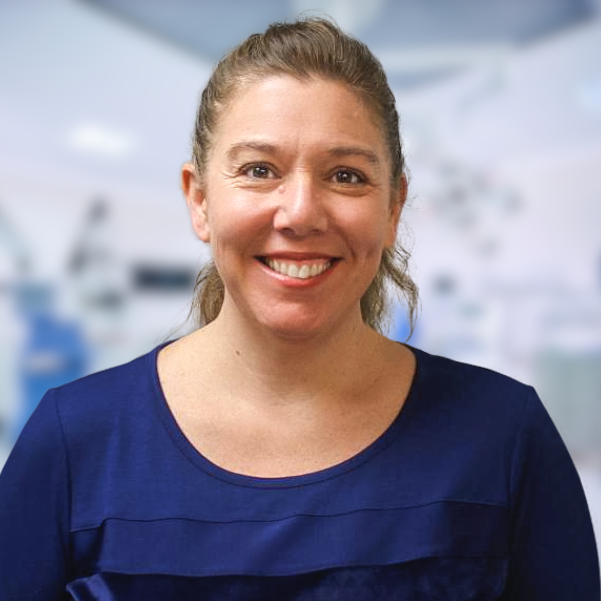 Woman with light brown hair smiles in a dark blue top, medical setting.