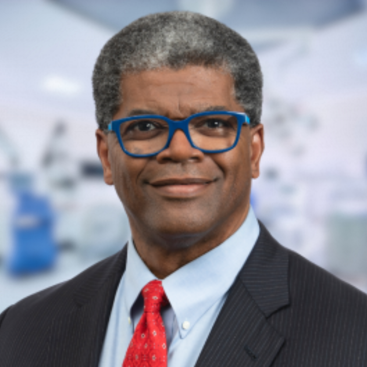 Man with glasses and a red tie smiling.