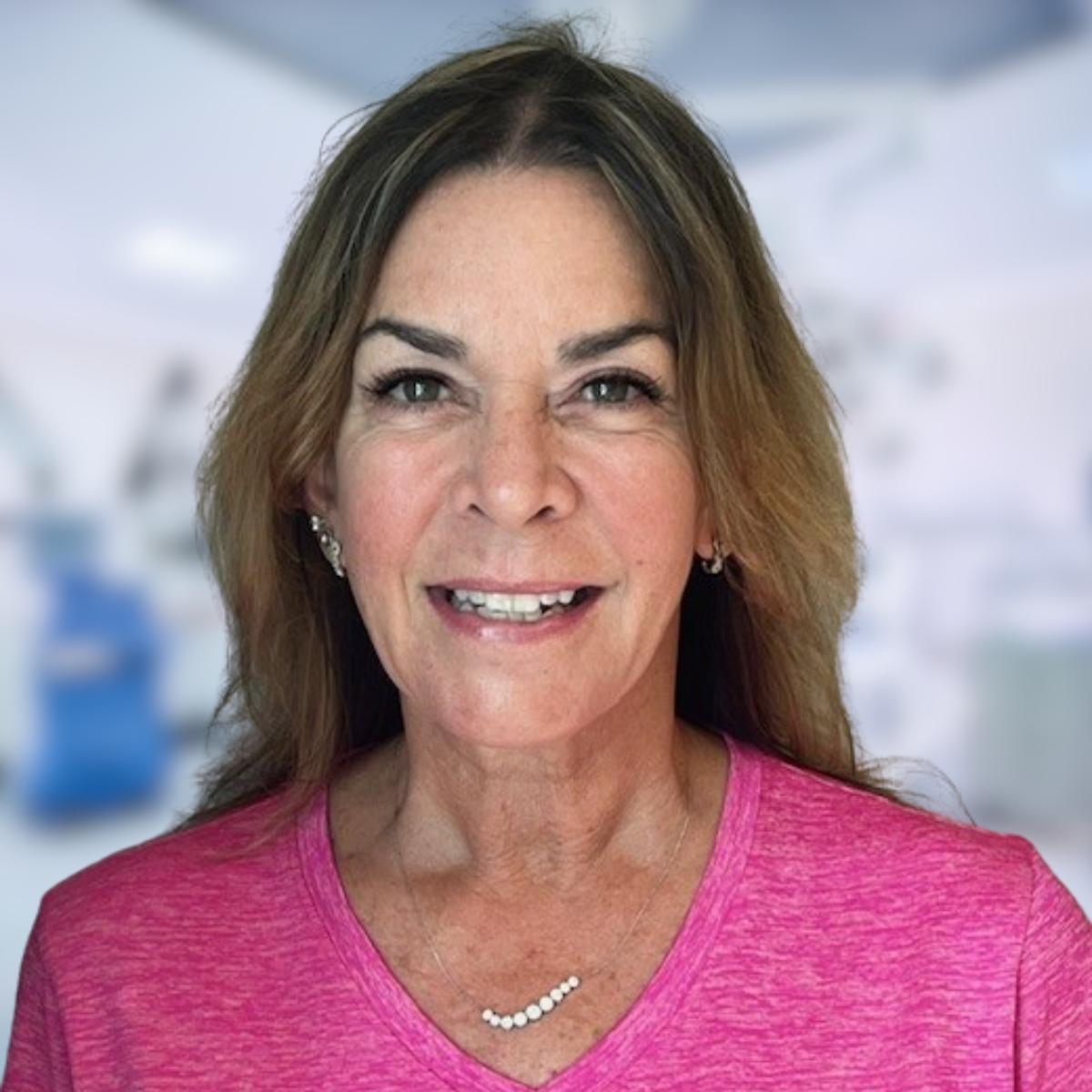 Woman with light brown hair smiles in a dark blue top, medical setting.