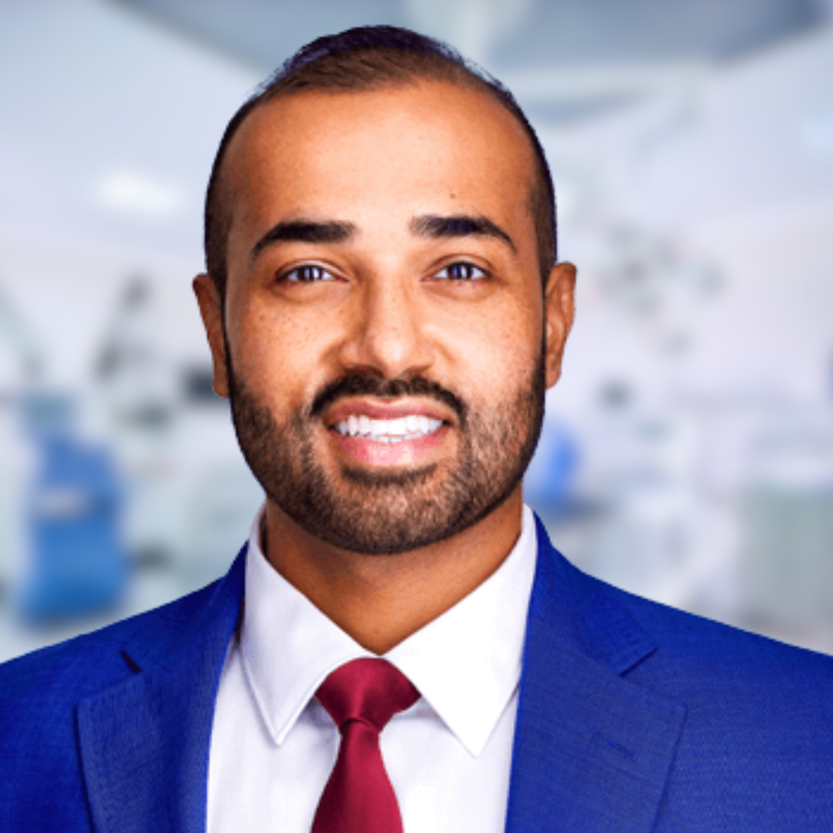 Smiling man in a blue suit and red tie, set in a blurred medical office.