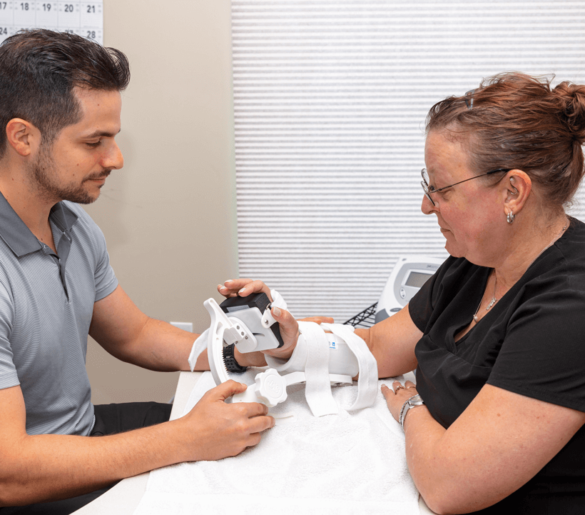 A man assists a woman with a hand brace in a medical setting.