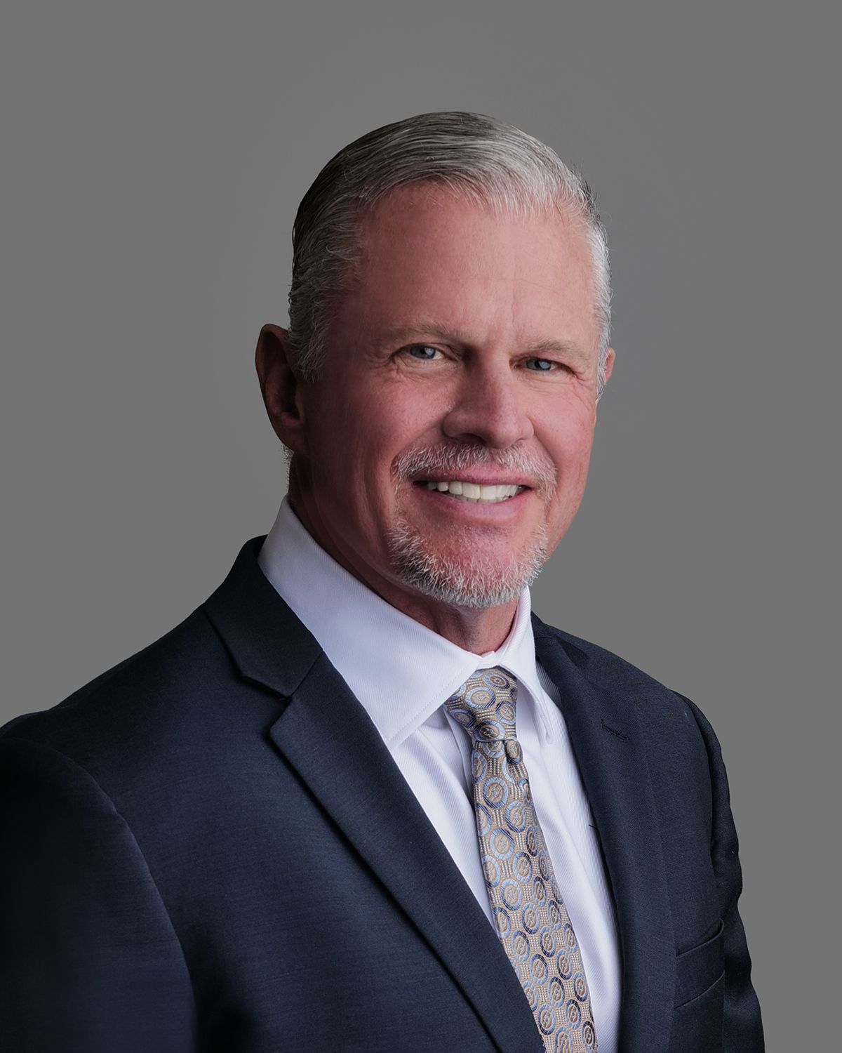 Man in suit smiling; blurred operating room background.