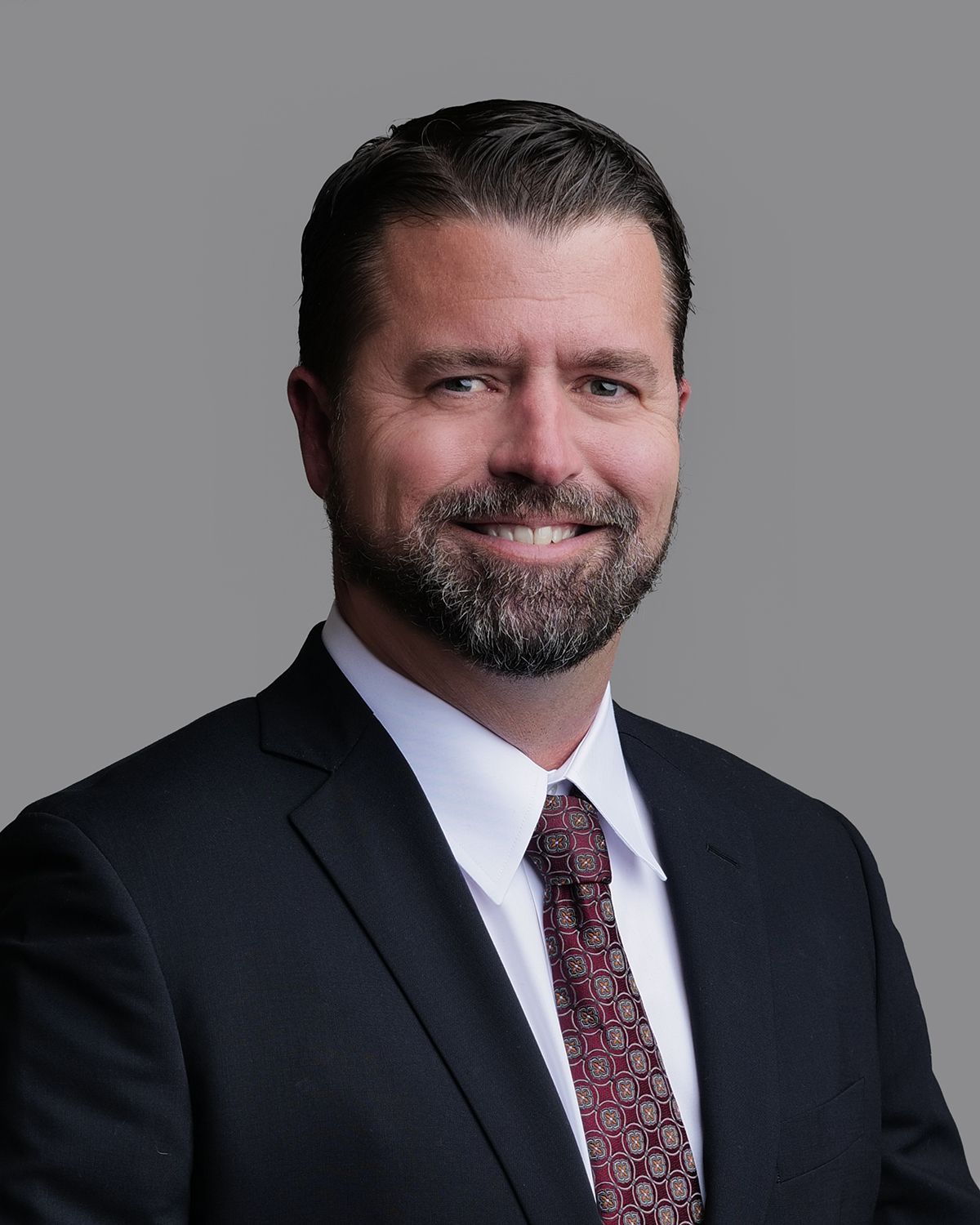 Man in dark suit smiles, with a medical setting blurred in background.
