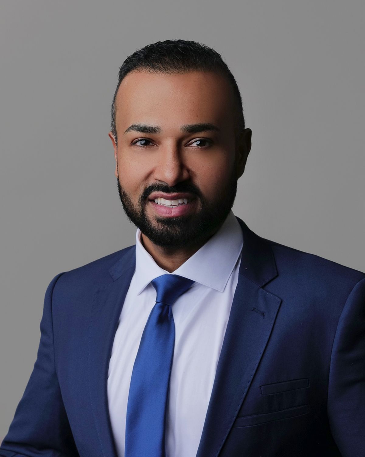 Smiling man in a blue suit and red tie, set in a blurred medical office.
