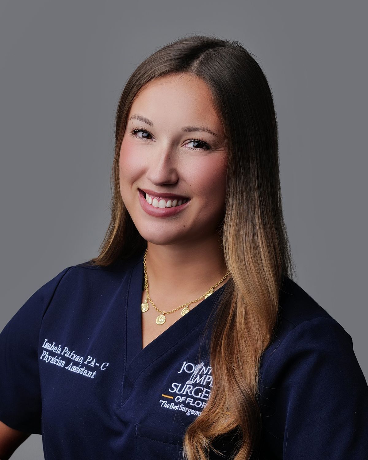 Woman in white lab coat smiling, likely a healthcare professional, in a blurred medical setting.