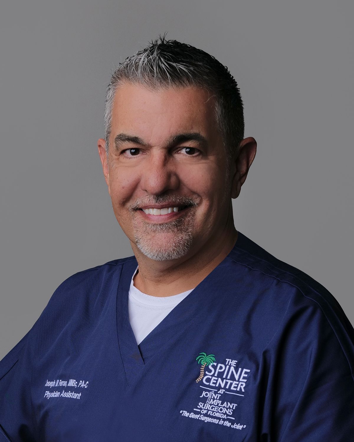 Man in a suit smiles at the camera; background is a blurred hospital setting.
