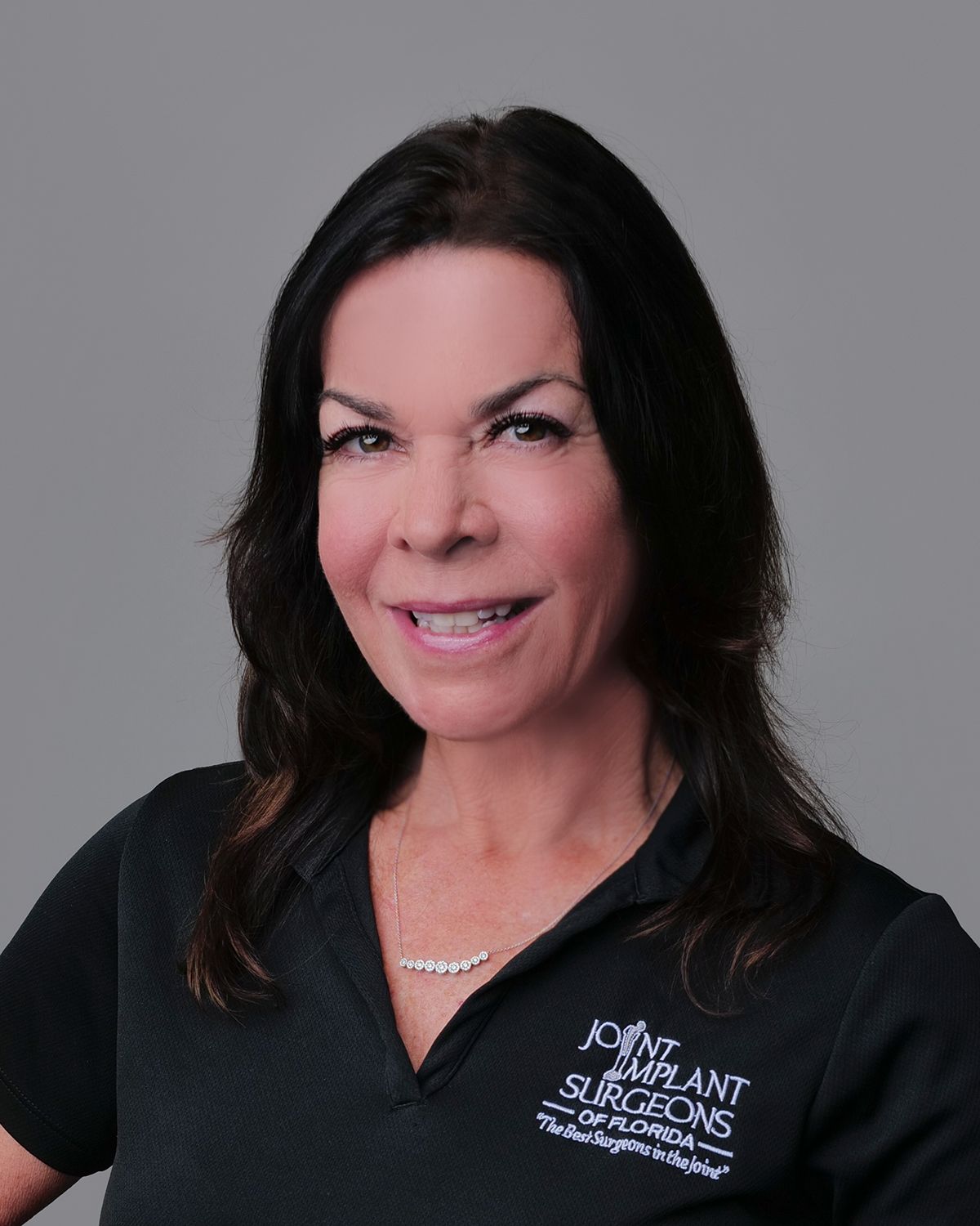 Woman with light brown hair smiles in a dark blue top, medical setting.