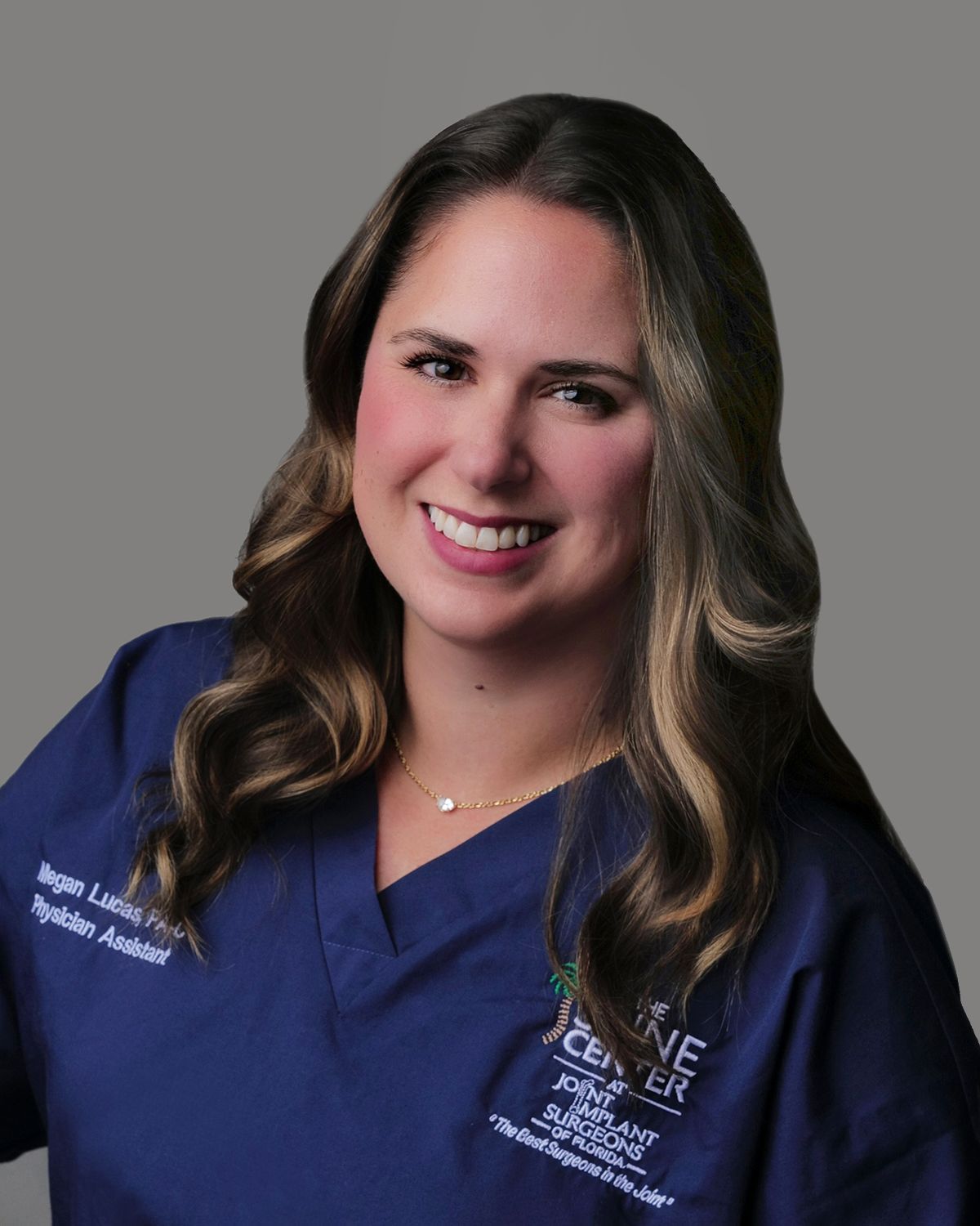 Woman with brown hair smiles at camera. She wears a black polo shirt in a medical setting.
