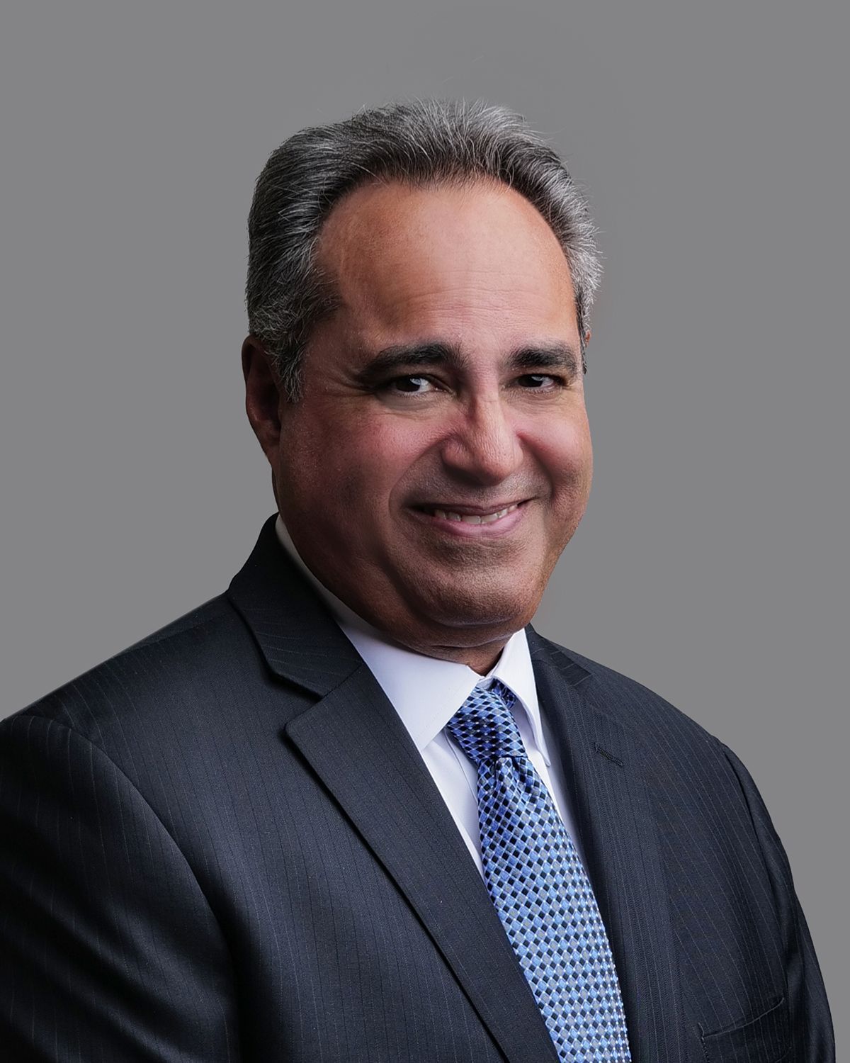 Smiling man in a suit and tie, possibly a doctor, in a blurred medical setting.