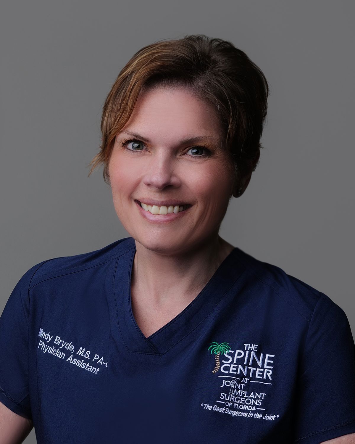 Female doctor with short brown hair, smiling, wearing a lab coat with 